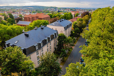 Das Bild zeigt das Hotel am Schosspark von oben umgeben von gr&uuml;nen B&auml;umen ´
