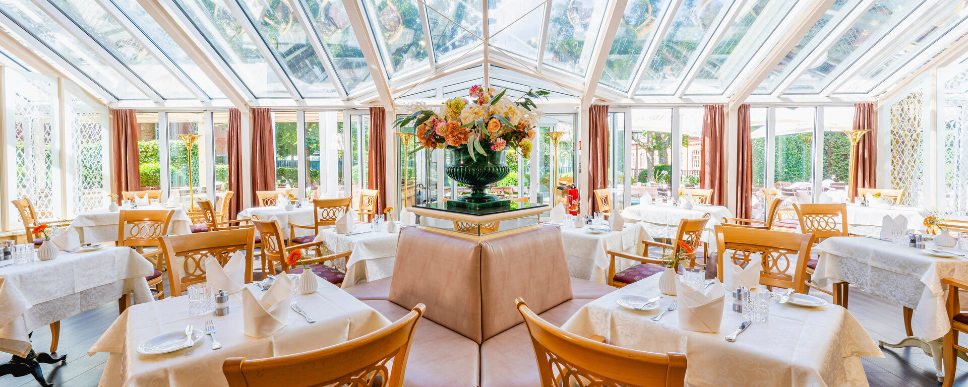In einem Wintergarten eines Hotels stehen gedeckte Tische.